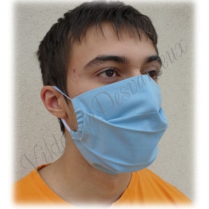 May include: A person wearing a light blue face mask with white elastic straps. The mask has multiple pleats and is made of a soft, breathable fabric.