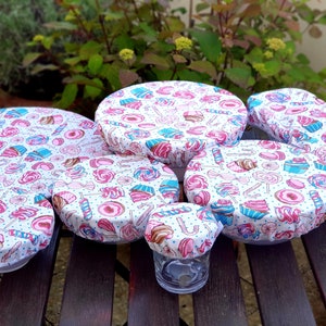 Könnte beinhalten: Ein Set mit sechs wiederverwendbaren Silikon-Lebensmittelbehältern mit einem rosa, blauen und weißen Süßwaren- und Cupcake-Muster. Die Abdeckungen bestehen aus einem dehnbaren Silikonmaterial und sind so konzipiert, dass sie auf Schalen und Behälter verschiedener Größen passen.