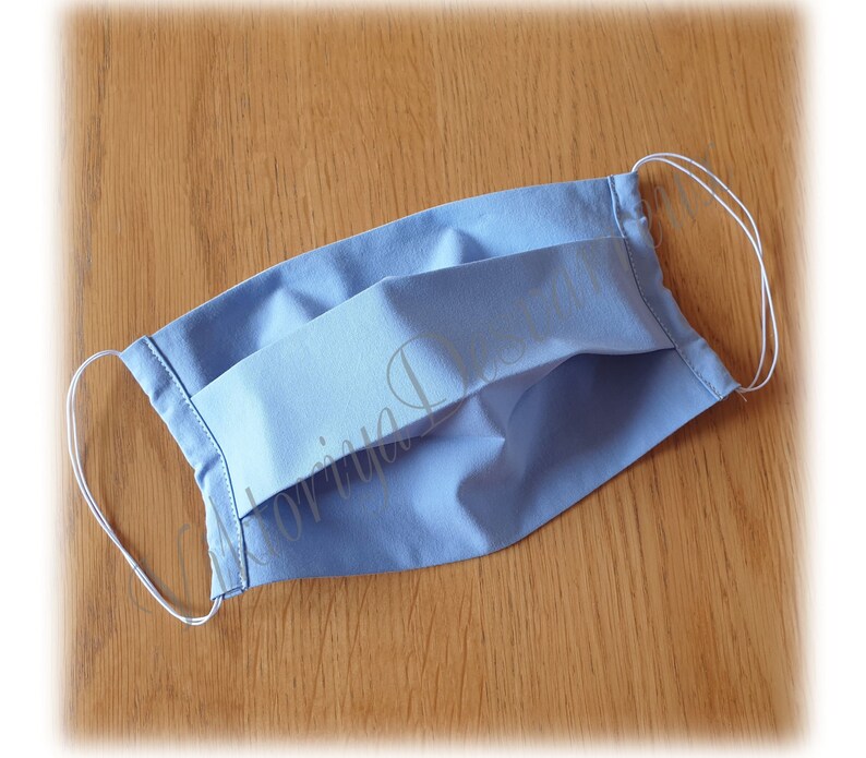 May include: A light blue pleated fabric face mask with white elastic ear loops.