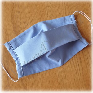 May include: A light blue face mask with white elastic ear loops. The mask is made of a soft, breathable fabric and has pleats for a comfortable fit.