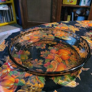 May include: A clear glass pie plate with a brown rim sits on a black tablecloth with a floral pattern featuring orange, yellow, and red flowers.