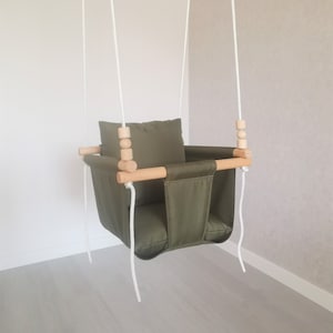 May include: A green fabric baby swing with a wooden frame and white ropes. The swing has a padded seat and a headrest.