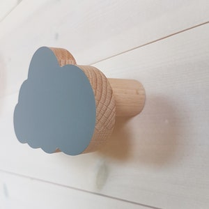 Puede incluir: Un gancho de pared de madera con forma de nube con una superficie pintada de azul claro. El gancho está hecho de madera natural y tiene una base cilíndrica.