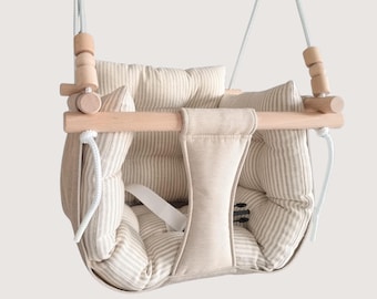May include: A hanging swing seat featuring a light beige and white striped fabric cushion with a central support strap. The structure is composed of smooth, light-colored wooden dowels and beads, suspended by thick white ropes on each side.