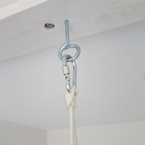 May include: A white rope is attached to a silver hook that is screwed into a white wooden beam. The rope is tied with a knot.