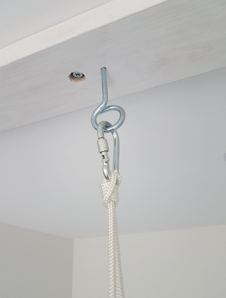May include: A white rope is attached to a silver hook that is screwed into a white wooden beam. The rope is tied with a knot.