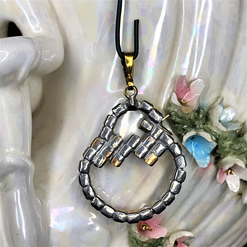 May include: A silver and gold pendant necklace with a mother of pearl center piece. The pendant is shaped like a circle with a geometric design.