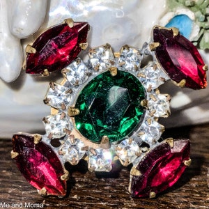 May include: A vintage brooch with a large green jewel surrounded by smaller clear rhinestones and four red jewels.
