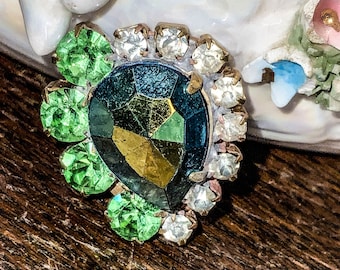 May include: A vintage brooch with a large, faceted, iridescent green, blue, and gold stone surrounded by a halo of clear rhinestones and smaller green stones.