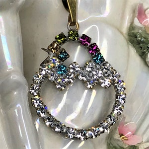 May include: A silver pendant with a clear crystal heart design. The heart is surrounded by a rainbow of colored crystals.