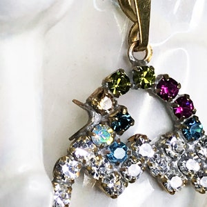 May include: A gold pendant with a heart-shaped design, featuring a rainbow of colorful rhinestones. The pendant is adorned with clear, green, blue, pink, and iridescent stones.