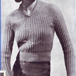 May include: A woman wearing a gray ribbed knit sweater with a V-neck collar. The sweater has a cropped length and long sleeves.