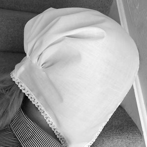 May include: A white cotton bonnet with lace trim. The bonnet is gathered at the top and has a simple, classic design.