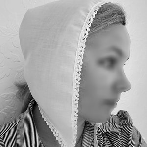 May include: A white cotton bonnet with a lace trim. The bonnet is worn by a person with their hair pulled back.