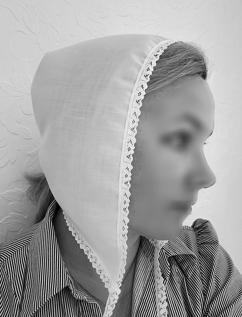 May include: A white cotton bonnet with a lace trim. The bonnet is worn by a person with their hair pulled back.