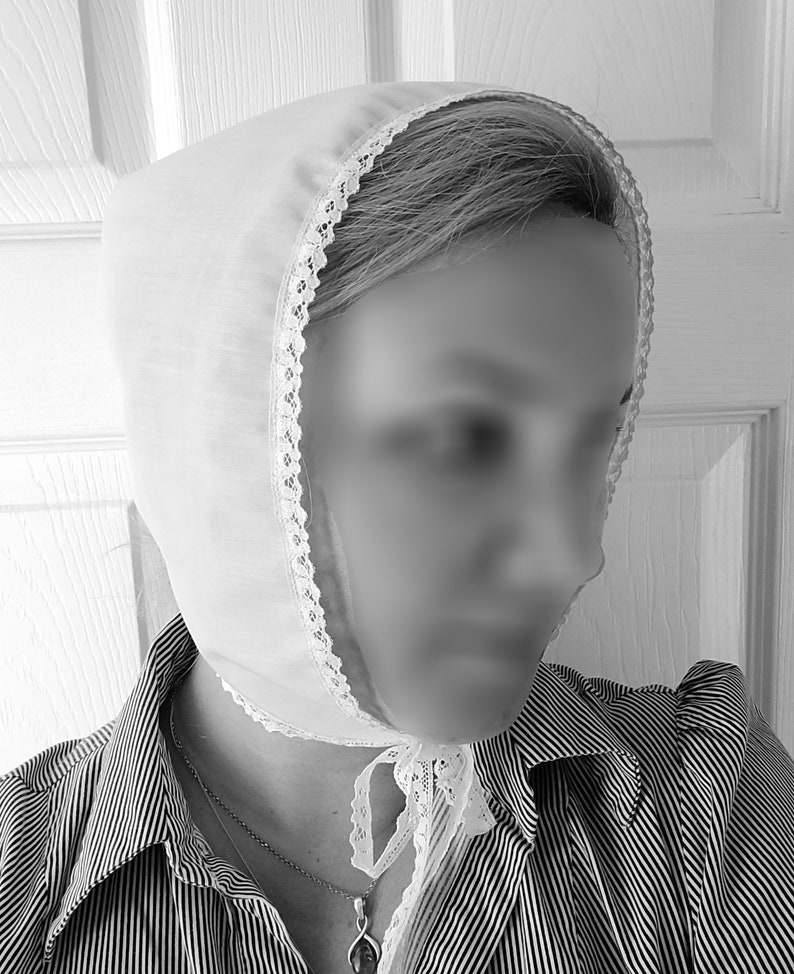 May include: A white cotton bonnet with lace trim, worn over a striped shirt. The bonnet has a bow tied at the back of the neck.