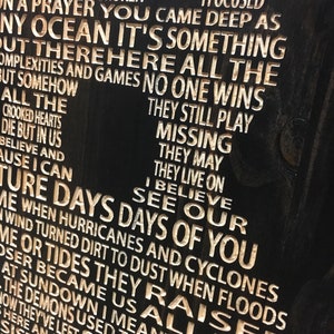 May include: A dark wooden plaque with carved white lettering. The text includes phrases like "Days of You," "When I was feeling broken," and "No One Wins." The overall theme appears to be inspirational or reflective.