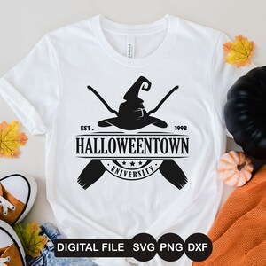 K&ouml;nnte beinhalten: Ein wei&szlig;es T-Shirt mit einem schwarzen Grafikdesign eines Hexenhutes mit gekreuzten Besen. Die Grafik enth&auml;lt auch den Text "EST. 1998 HALLOWEENTOWN UNIVERSITY".