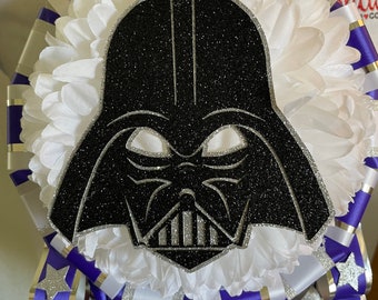 Puede incluir: Una banda de graduación blanca y morada con una máscara de Darth Vader negra y plateada con purpurina en el centro. La banda tiene rayas blancas y moradas y una estrella plateada en el lateral.
