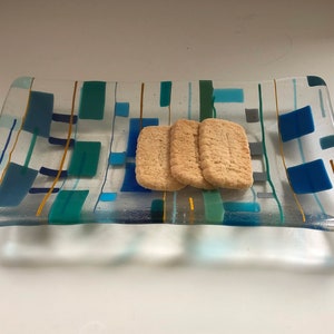 May include: A rectangular glass dish with a geometric pattern in shades of blue, green, and yellow. Three rectangular biscuits are on the dish.