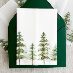 May include: A white card with a watercolor illustration of a forest scene. The card is inside a dark green envelope. The card has a white background with a row of five green trees in the center. The trees are painted in a watercolor style with a light green and dark green color scheme. The trees are surrounded by a light gray fog. The card is blank and ready for a message.