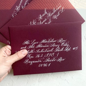 May include: Burgundy envelopes with white calligraphy addressing them to different recipients. The top envelope reads "DD Brenneman, Pevard, Unit 1012". The middle envelope reads "Like Korech, Dlanie Henderson, Unit L". The bottom envelope reads "Mr. Luis Montalvo Rios and Mrs. Monica Perez Ortiz,  Hitti Industrial Park Rd. #5, Km. 26.2, STE 1, Bayamon, Puerto Rico 00961".