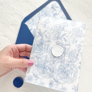Puede incluir: Un sobre blanco con un patr&oacute;n floral azul y un sello de cera blanco. El sobre est&aacute; siendo sostenido por una mano.