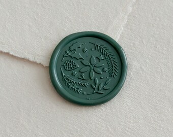 May include: A dark green wax seal with a botanical design featuring a pinecone, leaves, and a flower. The seal is circular and sits on a light-colored paper background. The design is embossed.