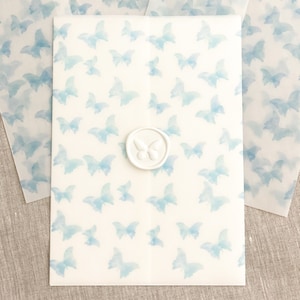 May include: A white envelope with a blue watercolor butterfly pattern. A white wax seal with a butterfly design is on the front of the envelope.