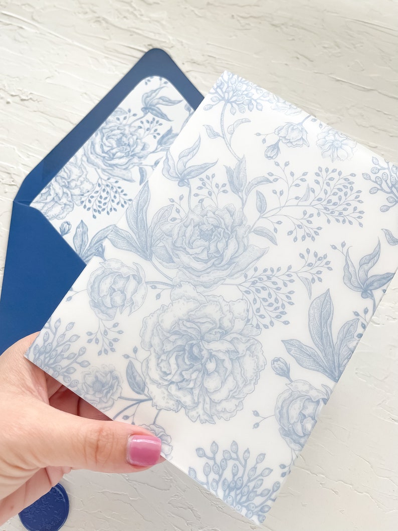 Puede incluir: Un sobre con estampado floral azul sobre fondo blanco. El sobre est&aacute; doblado por la mitad y se sostiene en una mano.