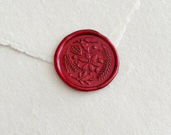May include: A round, red wax seal with a floral design, including a pinecone and leaves, is placed on a textured, off-white paper. The seal's intricate details and rich color contrast with the paper's soft, torn edge, creating an elegant aesthetic.