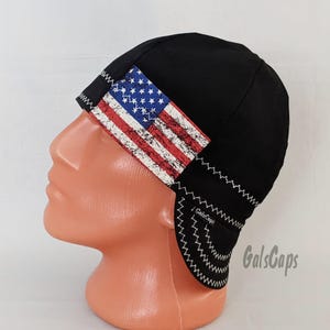 May include: Black welding cap with a distressed American flag design on the side. The cap has a white zig-zag stitch around the edge and the text "GalsCaps" is visible on the side.
