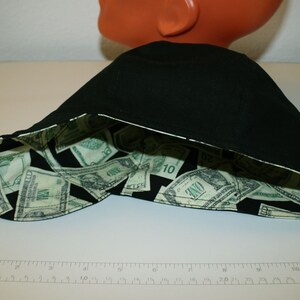 May include: Black baseball cap with a white trim. The interior lining features a pattern of US dollar bills. The cap is displayed on a white surface.