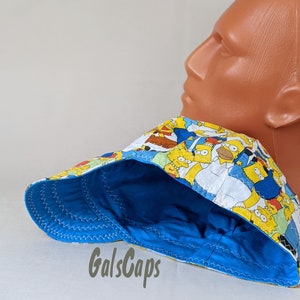 May include: A blue and yellow baseball cap with a cartoon print of characters from the Simpsons. The cap has a blue brim and a yellow crown.