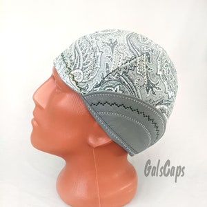 Può includere: Un berretto da saldatore a fantasia paisley grigio e bianco con una patta in pelle grigia. Il berretto è su una testa di manichino. Il testo "GalsCaps" è visibile nell'angolo in basso a destra dell'immagine.