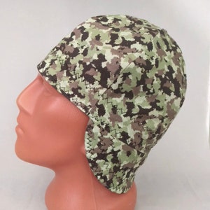 May include: A green, brown, and white camouflage welding cap with ear flaps.