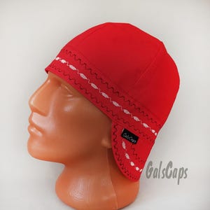 May include: A bright red welding cap with white decorative stitching along the brim and ear flaps. The cap is displayed on a mannequin head. The brand name "GalsCaps" is visible on the cap.
