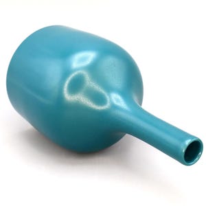 May include: A teal-colored ceramic vase with a rounded body and a long, slender neck. The vase has a smooth, glossy finish and is set against a white background. The design is simple and modern.