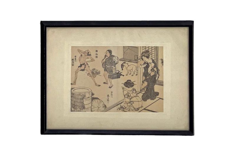 Op de afbeelding: Een ingelijste Japanse houtsnede die een sc&egrave;ne afbeeldt met verschillende figuren, waaronder een rennende man, een vrouw en een hond. Het kunstwerk is in zwart-wit, met een zwart frame en een cr&egrave;mekleurige passe-partout.