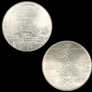 May include: A white ceramic mug with a black handle and the text "But First, Coffee" in a bold, black font. The mug is set against a blurred background, suggesting a cozy setting.