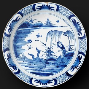 May include: A round, antique ceramic plate with a blue and white landscape design. The plate features a central scene of figures near water, surrounded by a decorative border. The plate measures approximately 10 inches in diameter.