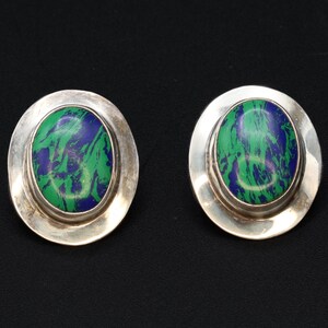 Pode incluir: Um par de brincos de botão ovais. Cada brinco apresenta uma moldura prateada polida em torno de uma pedra com um padrão marmorizado verde e azul. Os brincos são exibidos em um fundo preto.