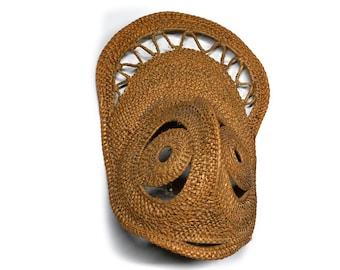 May include: A woven mask with a brown hue, featuring a circular design at the top and spiral patterns. The mask has openings for the eyes and mouth, and is likely used for ceremonial or decorative purposes.