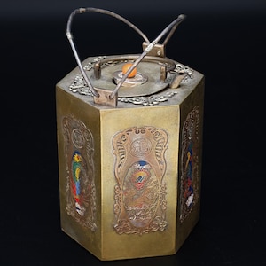May include: An antique, hexagonal metal teapot with ornate relief panels. The panels feature colorful bird and dragon designs. The teapot has a silver handle and a small, orange knob on the lid. The overall color is gold with silver accents.