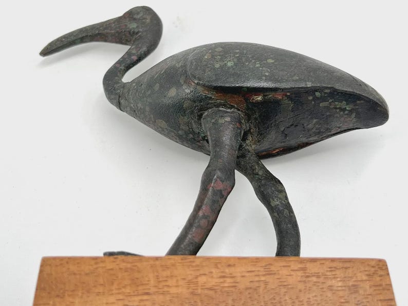 Peut inclure: Sculpture d'oiseau en bronze avec un long bec incurv&eacute; et des pattes fines. L'oiseau est pos&eacute; sur une base rectangulaire en bois. La sculpture a un aspect vieilli avec des reflets verts et rouges.