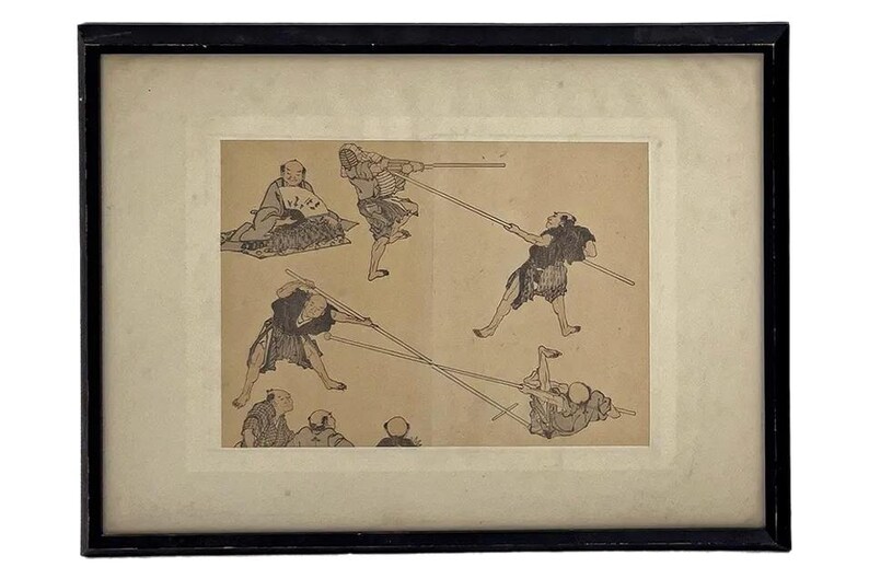 May include: Framed vintage print featuring several figures engaged in a martial arts practice with long poles. The artwork is in black and white, with a sepia-toned background. The print is set in a black frame with a white mat.