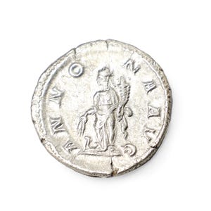 K&ouml;nnte beinhalten: Eine silberne r&ouml;mische M&uuml;nze mit einem detaillierten Relief einer Figur, die einen Stab und ein Weizenb&uuml;ndel h&auml;lt. Die M&uuml;nze hat sichtbare Inschriften am Rand und ist vor einem wei&szlig;en Hintergrund platziert. Die M&uuml;nze ist leicht abgenutzt.