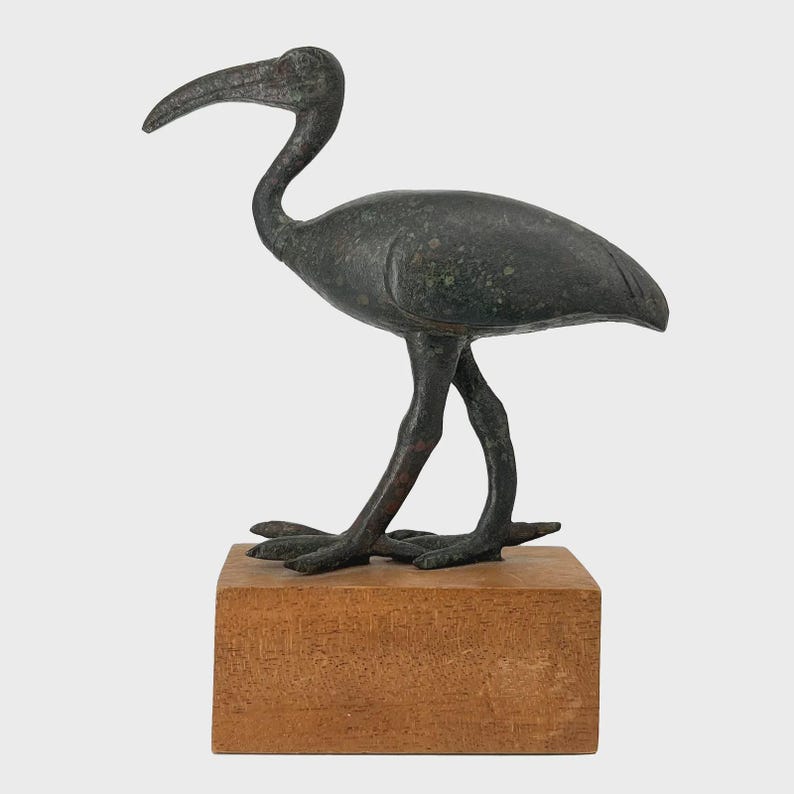 Peut inclure: Une sculpture d'oiseau en bronze avec un long bec courb&eacute; et des pattes fines, pos&eacute;e sur un socle rectangulaire en bois. Les plumes de l'oiseau sont d&eacute;taill&eacute;es, et la sculpture a un aspect vieilli et antique. La sculpture mesure environ 25 cm de haut.