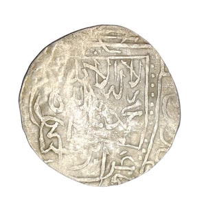 Puede incluir: Una moneda de plata con intrincada escritura &aacute;rabe. La moneda tiene una superficie desgastada y texturizada y una forma ligeramente irregular. El dise&ntilde;o presenta caligraf&iacute;a detallada y patrones geom&eacute;tricos.