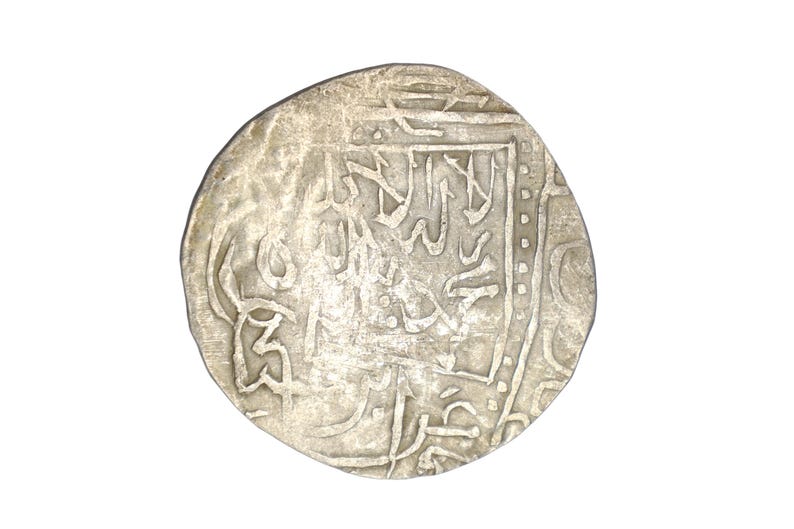 Puede incluir: Una moneda de plata con intrincada escritura &aacute;rabe. La moneda tiene una superficie desgastada y texturizada y una forma ligeramente irregular. El dise&ntilde;o presenta caligraf&iacute;a detallada y patrones geom&eacute;tricos.